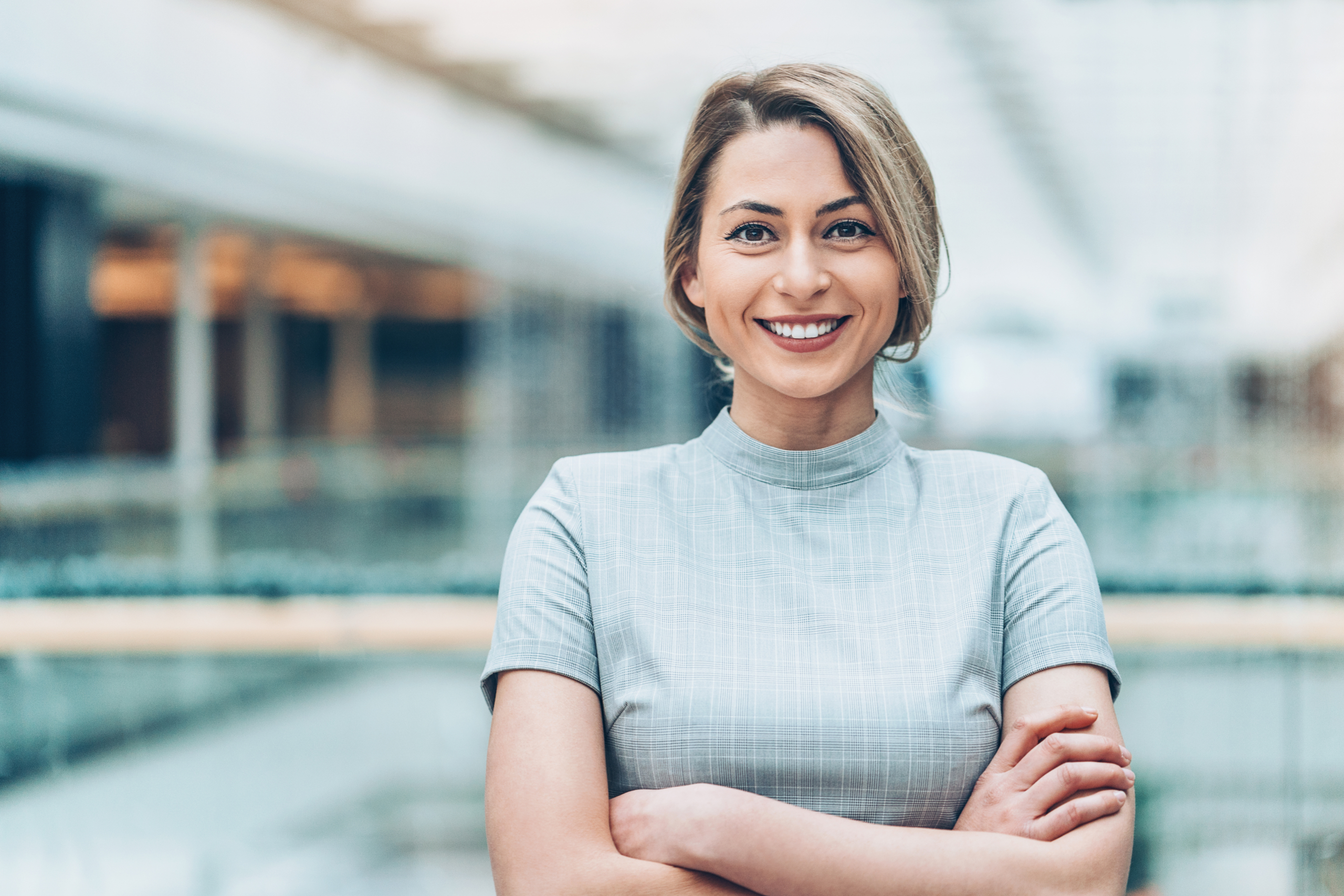 Foto einer selbstbewussten, lächelnden Frau mit verschränkten Armen